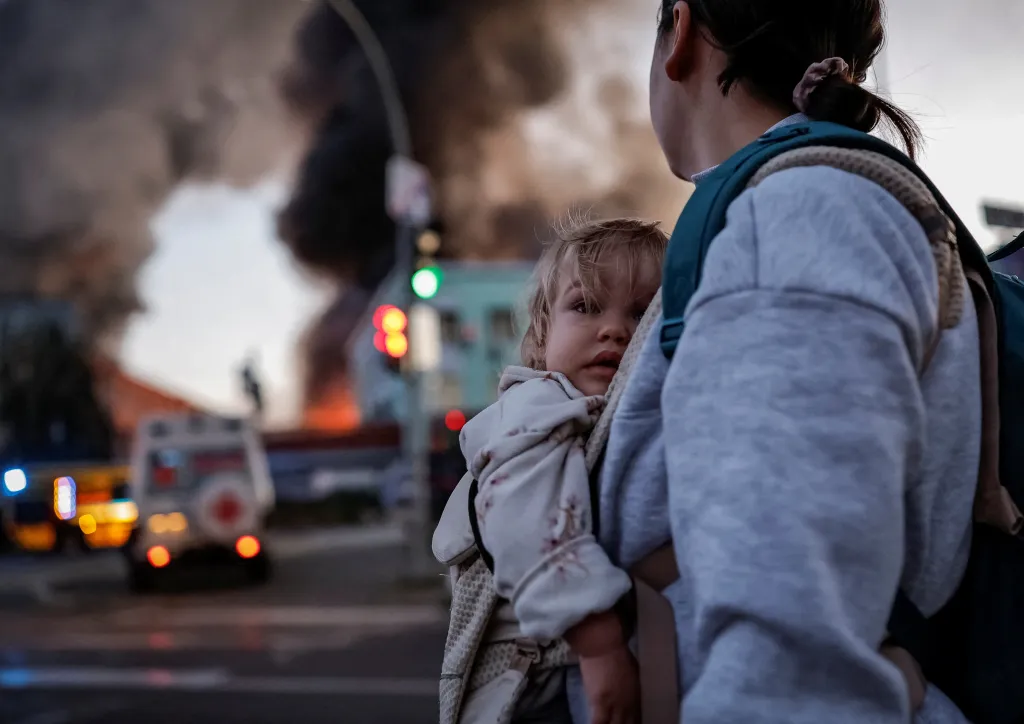 A woman carrying a child on her back at the site of a Russian missile strike in Kyiv.