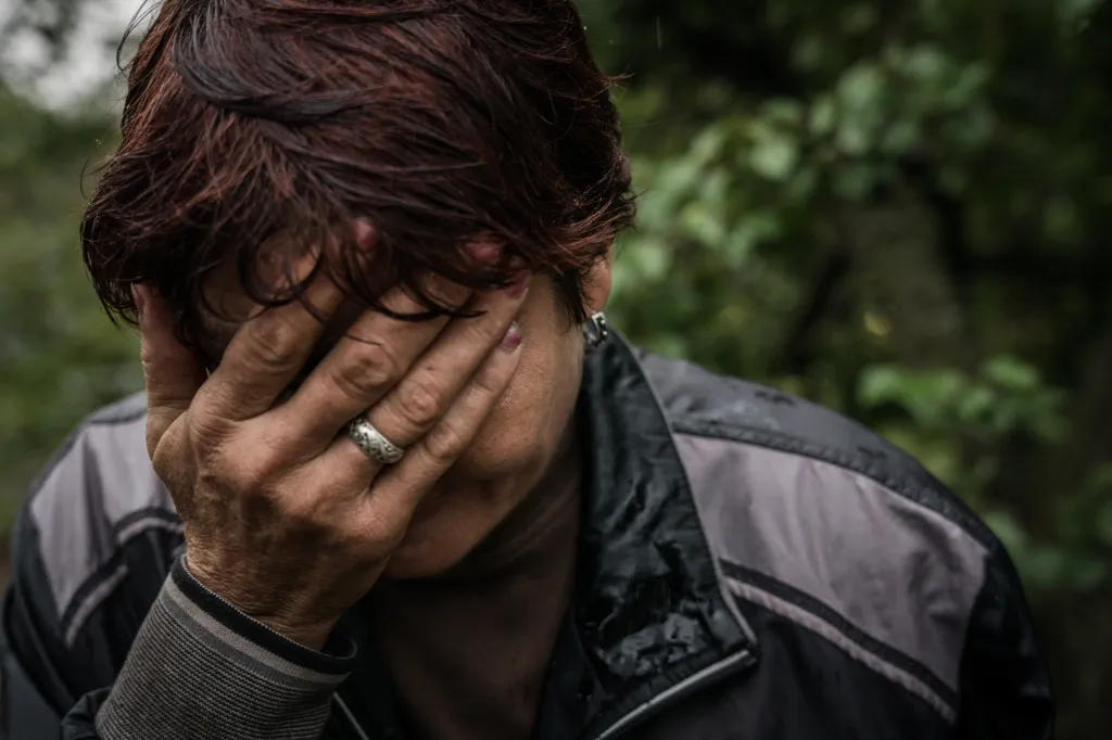 A woman covers her face with her hand, a silver ring visible on her ring finger.