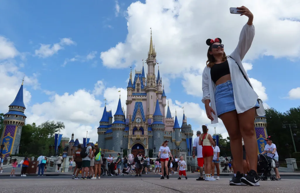 A woman wearing Minnie Mouse ears takes a selfie in front of Cinderella's Castle at Magic Kingdom Park.