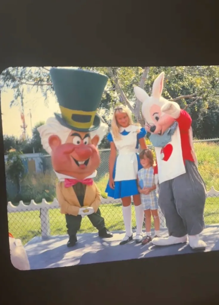 A vintage photo of a girl dressed as Alice from Wonderland, standing between the Mad Hatter and the White Rabbit.