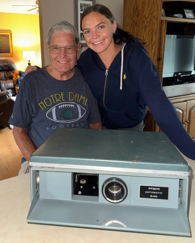 A woman and an older man stand behind an Argus Automatic 540 slide projector.