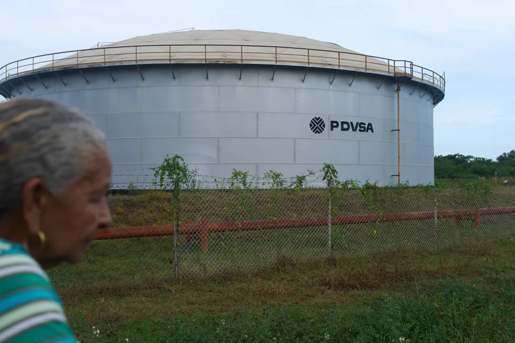 A woman walks past an oil storage tank with the PDVSA logo in Cabimas, Venezuela.