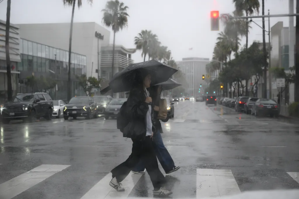 Two women holding umbrellas cross a street in Beverly Hills during heavy rain.