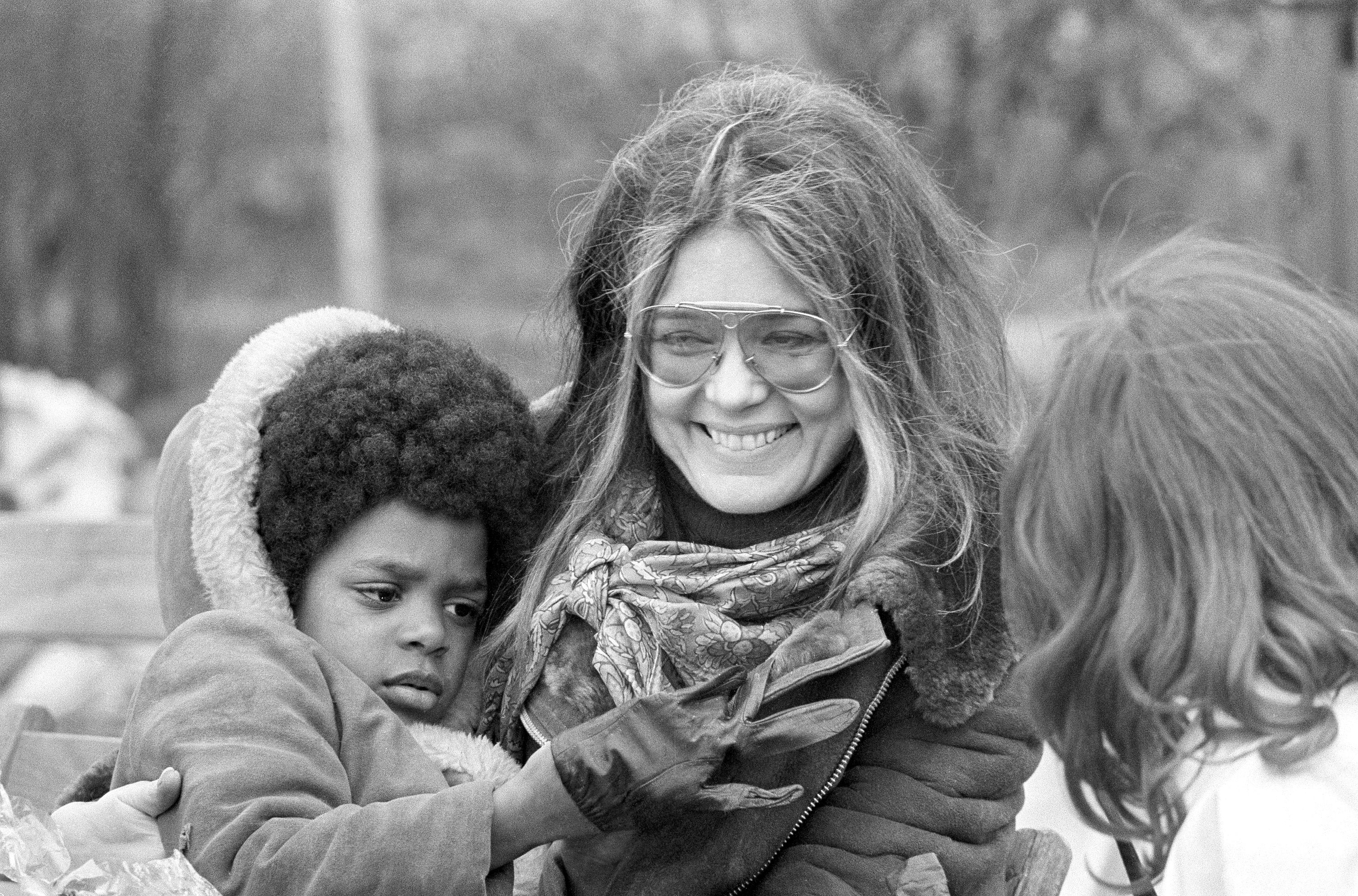 Gloria Steinem smiles wearing sunglasses next to a child with curly hair.