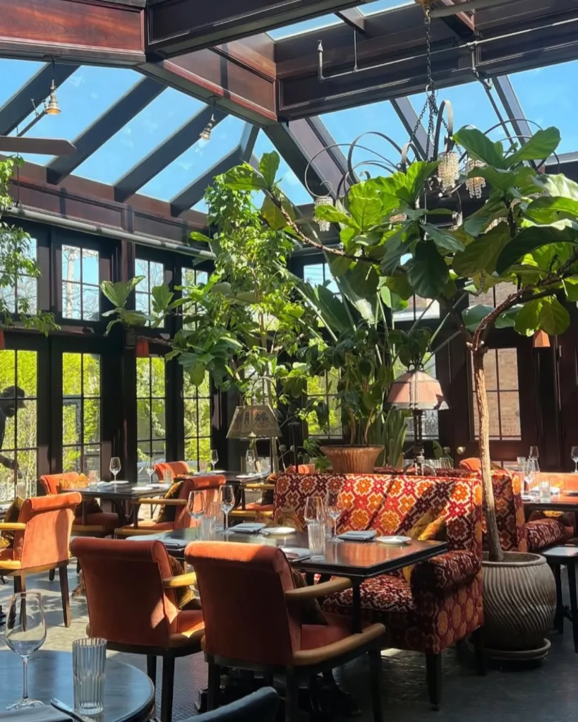 A conservatory restaurant with a glass roof and large leafy plants.