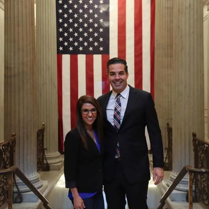 Jeffrey Small and Lauren Boebert posing in front of a large American flag.