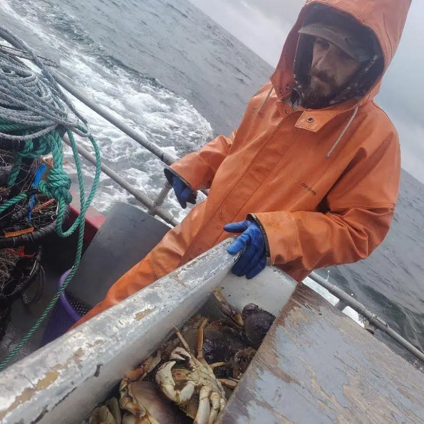 Todd Meadows in an orange raincoat and blue gloves, standing over a container of crabs on a boat.