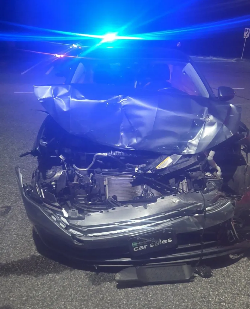 A totaled car with a heavily damaged front end, illuminated by blue flashing lights, suggesting a night time accident scene.