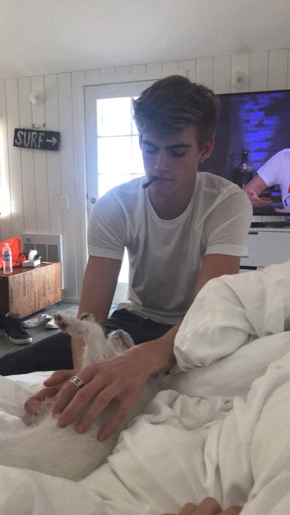 Presley Gerber petting a white dog while smoking a cigarette.