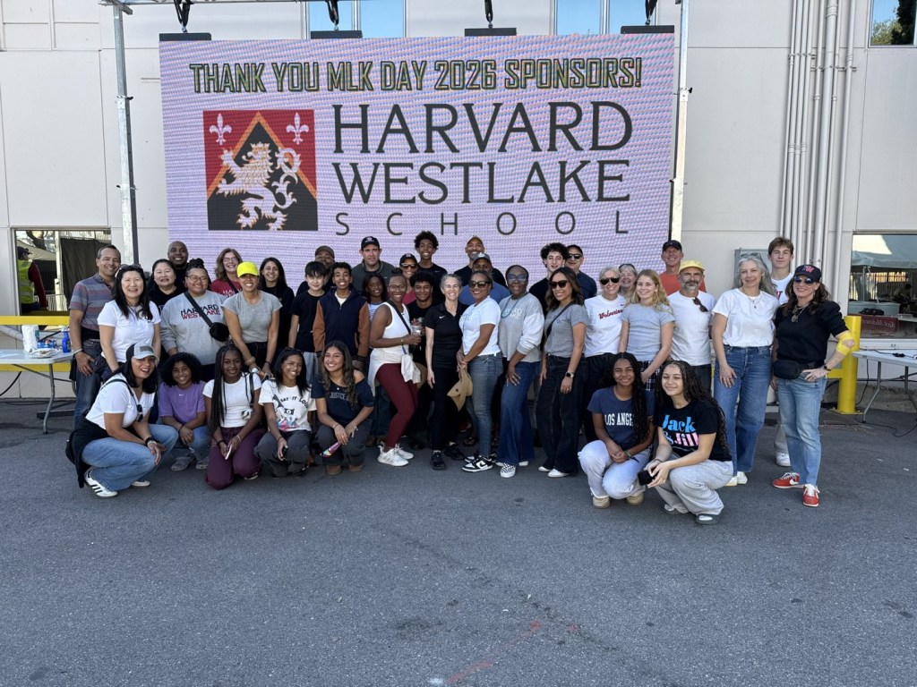 A large group of adults and young people posing in front of a screen displaying 