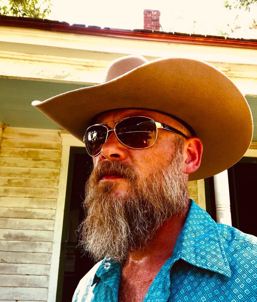 Dolly Parton's nephew, Bryan Seaver, in a tan cowboy hat, sunglasses, and a blue patterned shirt.