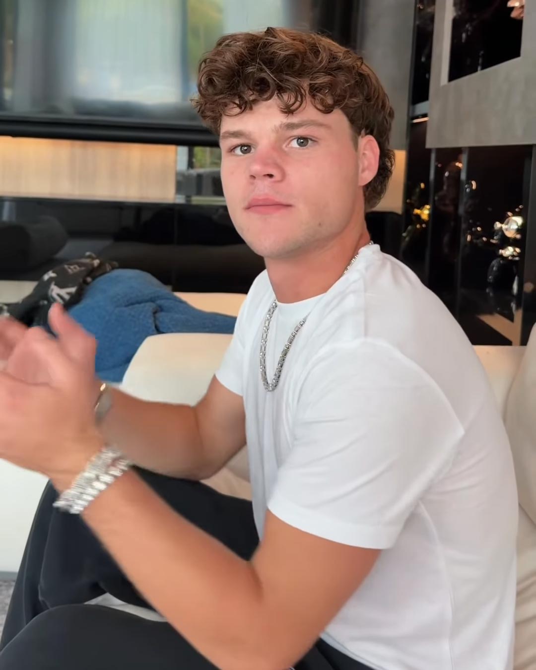 Jack Doherty, a young man with curly brown hair, wearing a white t-shirt and silver chain.
