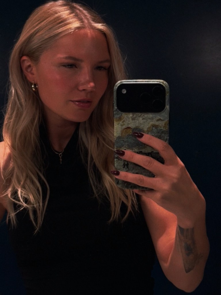 A woman with blonde hair taking a selfie in a mirror.
