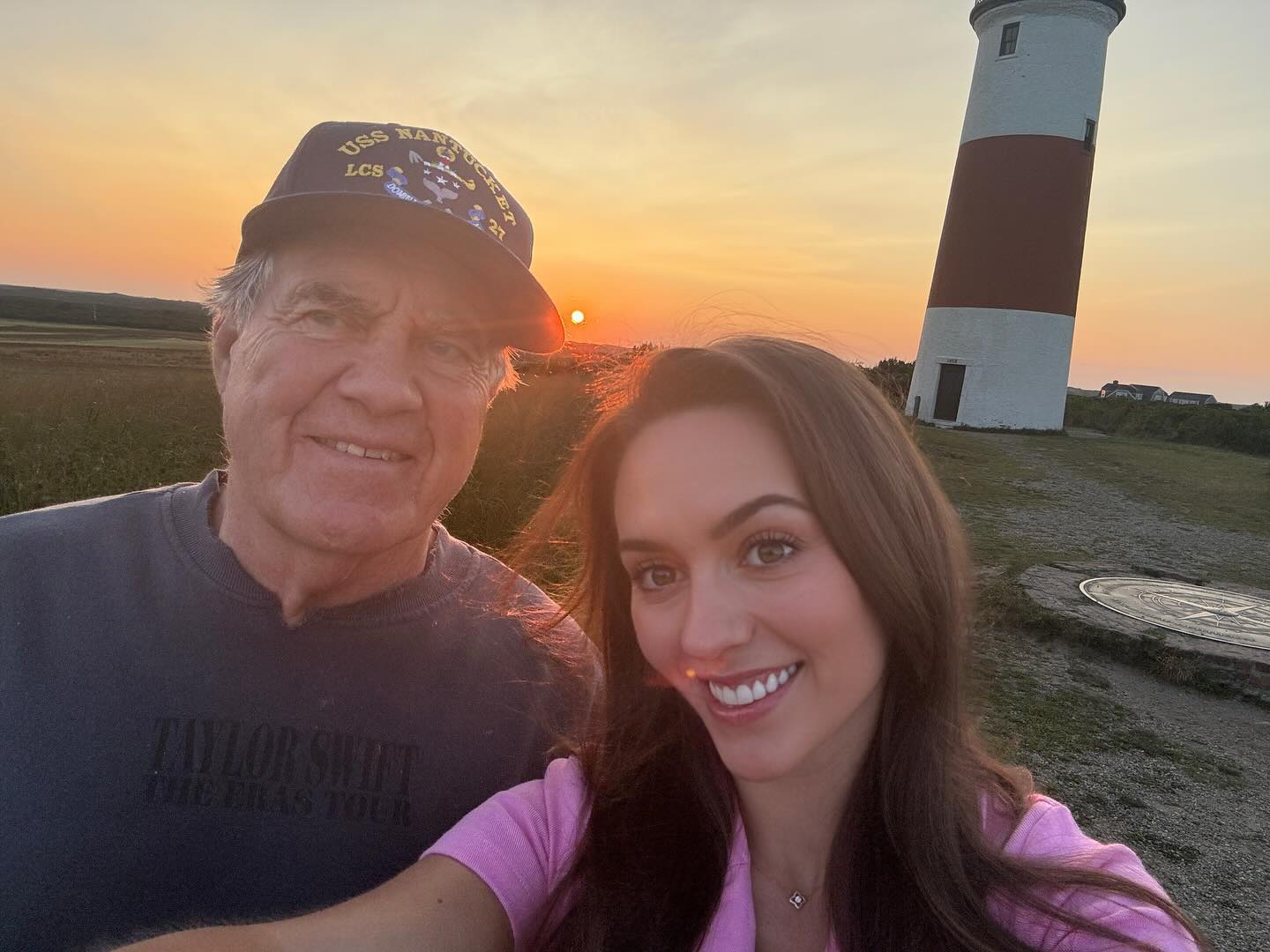 Jordon Hudson and Bill Belichick posing for a selfie in front of a lighthouse at sunset.