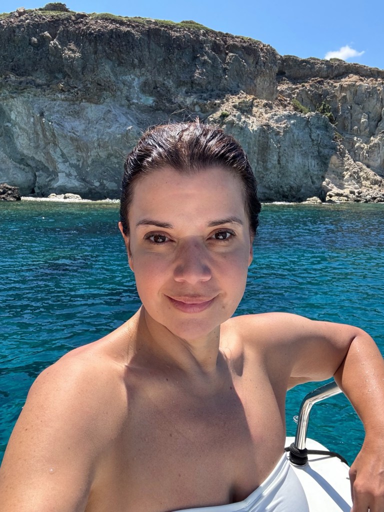 Ana Navarro on a boat in clear blue water, with rocky cliffs in the background.