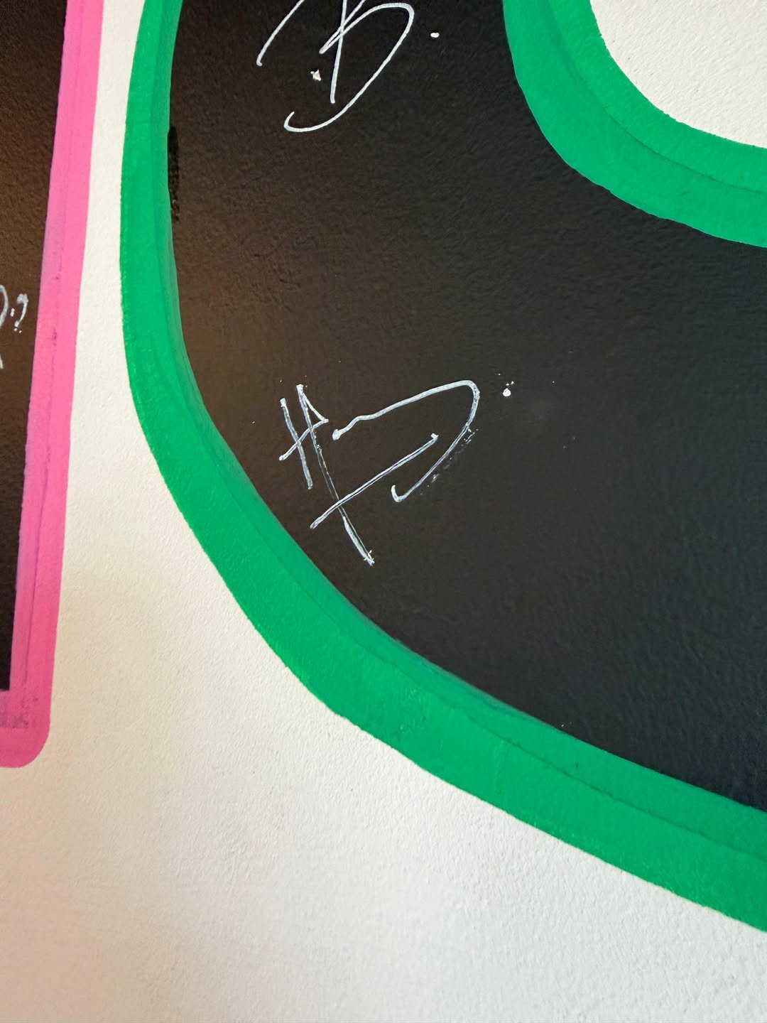 Wall with signatures on black, pink, and green painted sections.