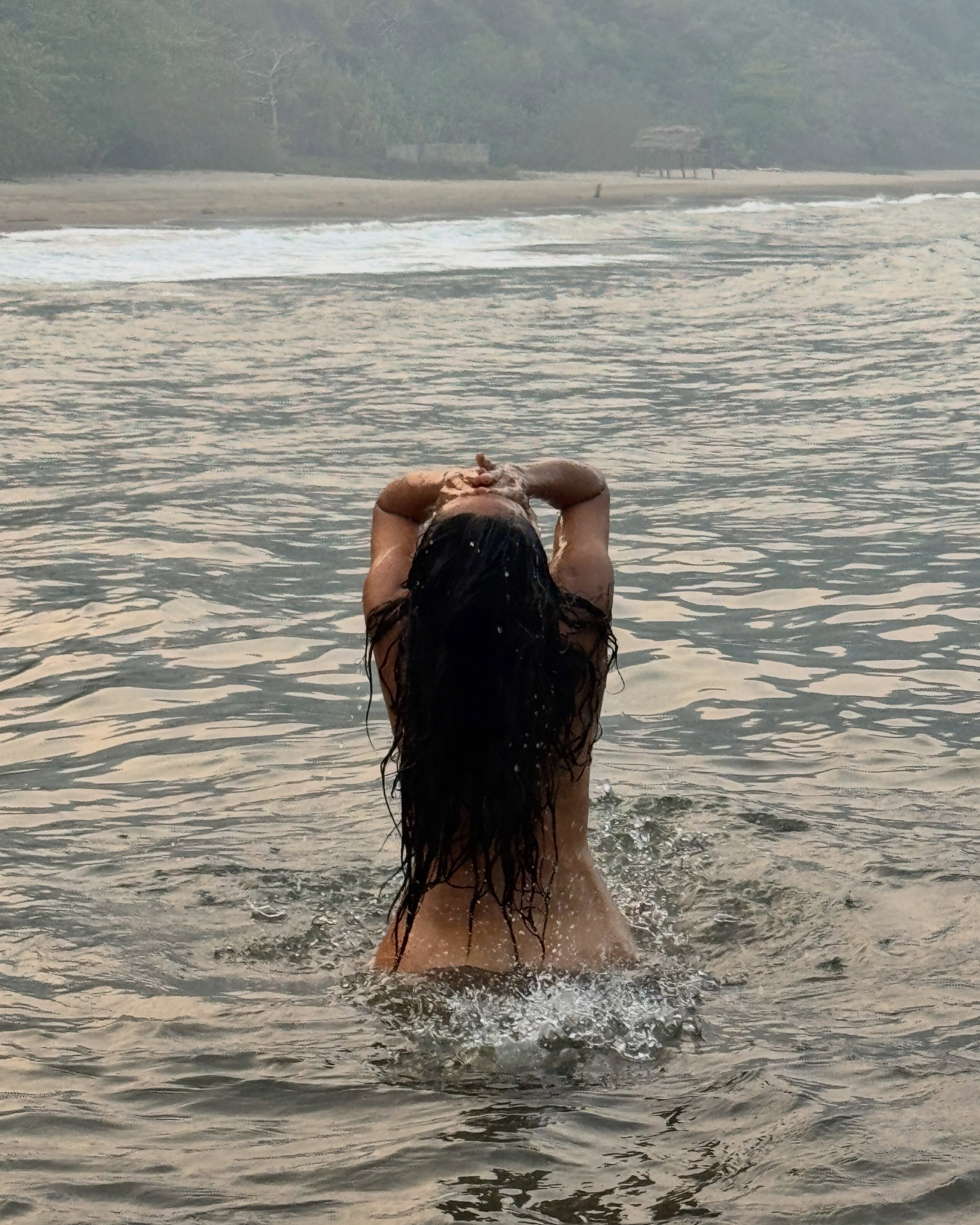Salma Hayek with her back to the camera, waist-deep in water, looking up at the sky.