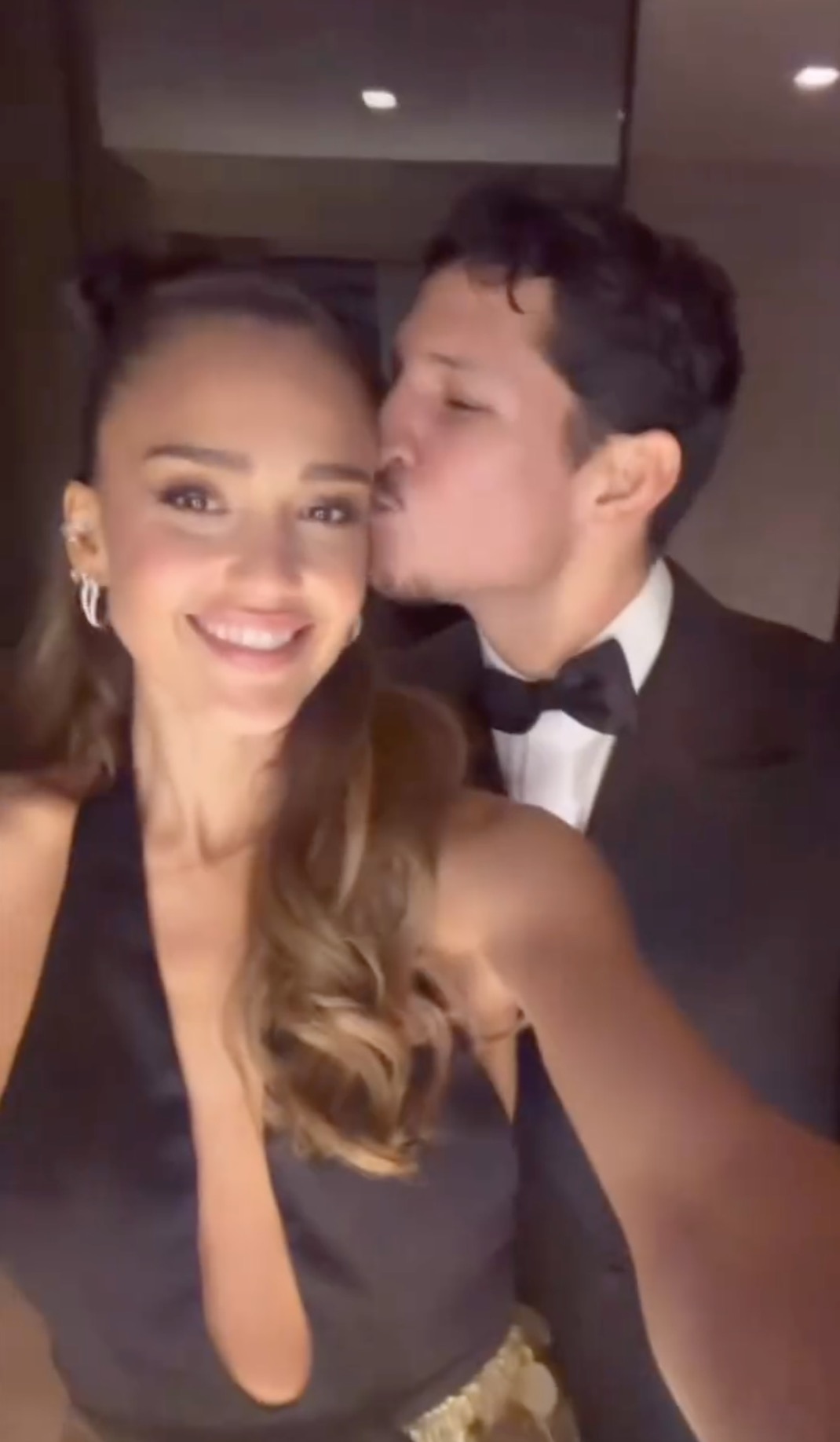 Jessica Alba smiling as she's kissed on the cheek by a man in a tuxedo.