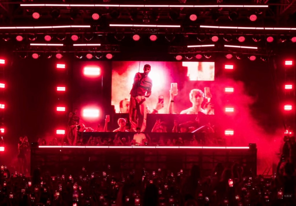 The Chainsmokers performing a concert at Discovery Meadow with red lighting and a large screen showing the performers.