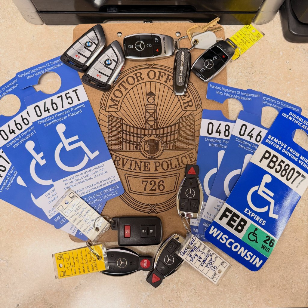 Multiple luxury car keys and disabled parking placards arranged on an Irvine Police Department emblem.