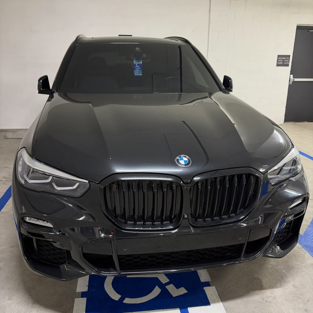 A black BMW SUV parked in a disabled parking spot with a fake disabled placard hanging from the rearview mirror.