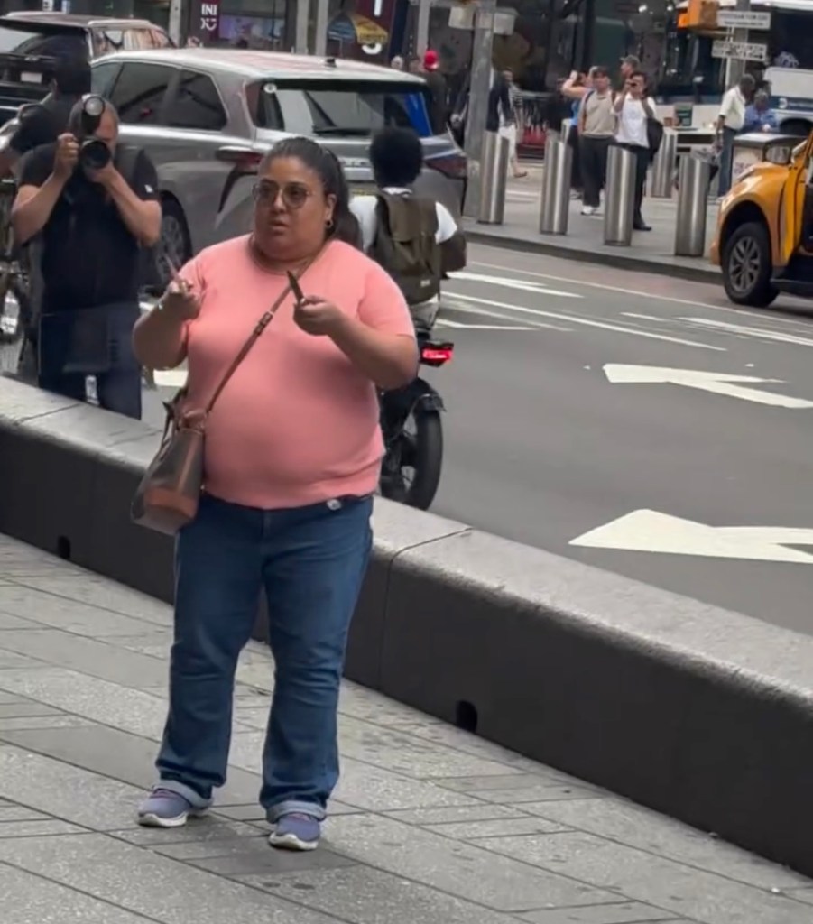 A woman in a pink shirt and jeans holding a knife, with a photographer in the background.