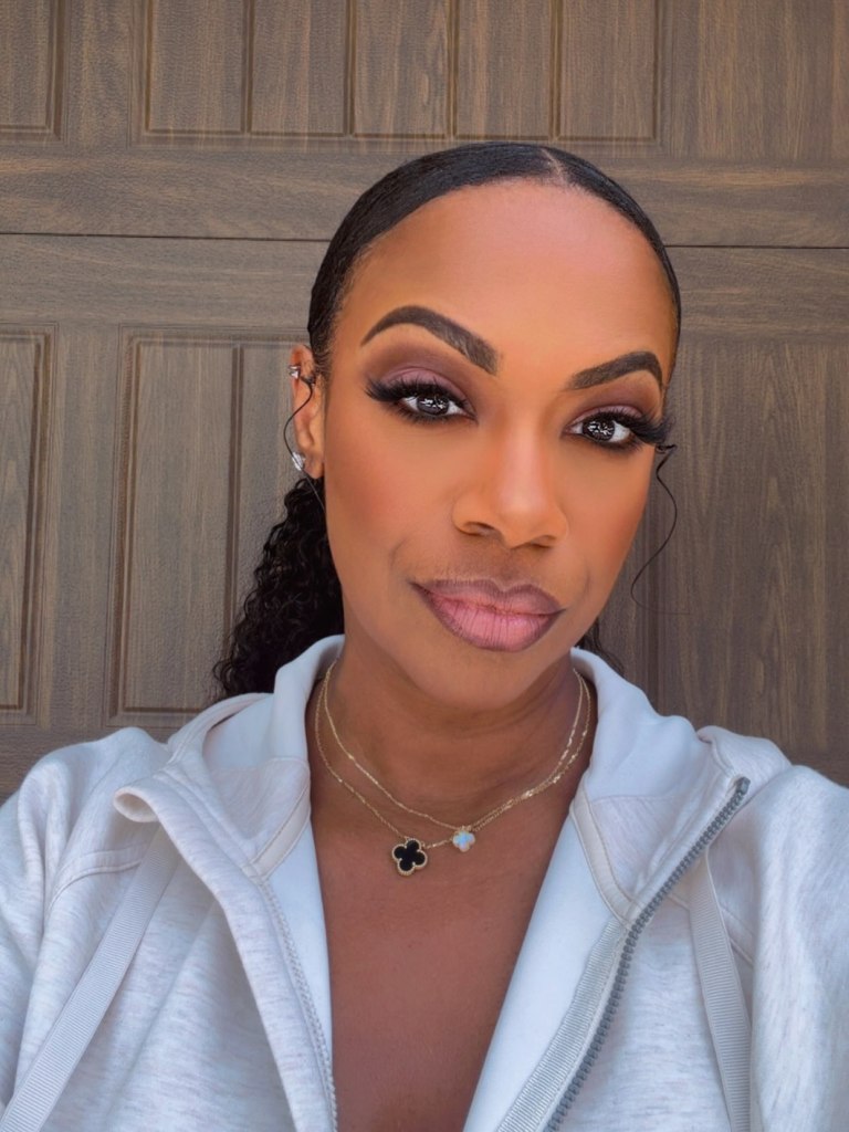 Kandi Burruss wearing a white zip-up hoodie, two necklaces, and dark eye makeup.