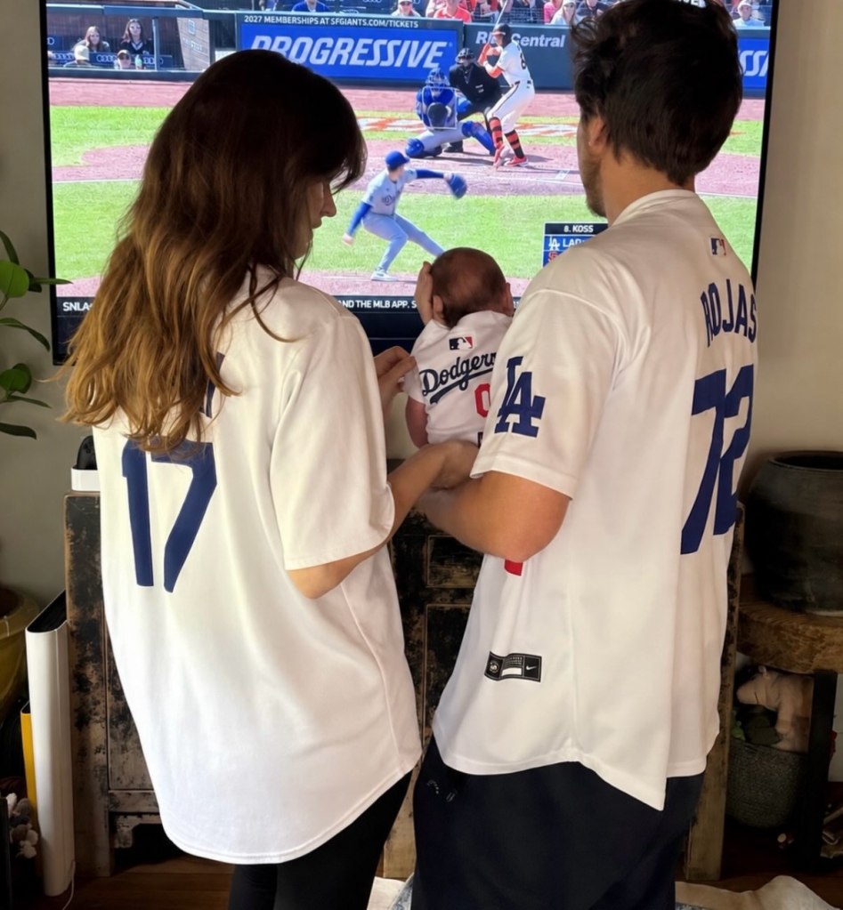 Barbara Palvin and Dylan Sprouse watching baseball with their baby.