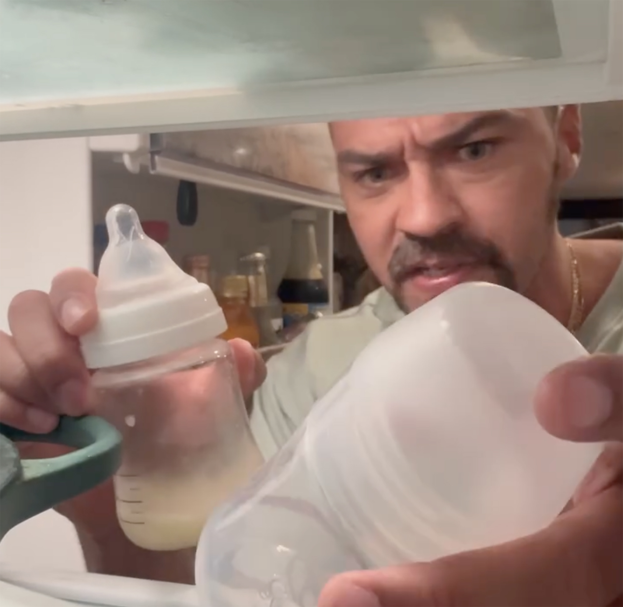 Jesse Williams holding two baby bottles in a refrigerator.