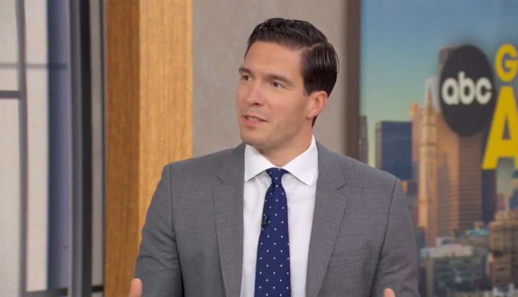 Will Reeve in a grey suit and a blue polka dot tie in front of a Good Morning America set.