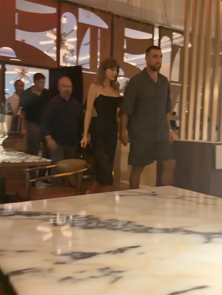 Taylor Swift and Travis Kelce hold hands while walking through a restaurant.