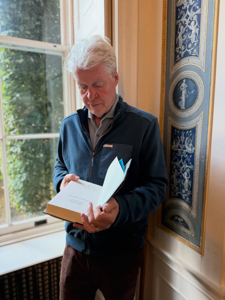 Charles Spencer, Princess Diana's brother, standing by a window and reading a book.