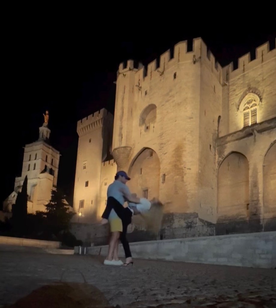 A man dips a woman in front of an illuminated medieval castle at night.