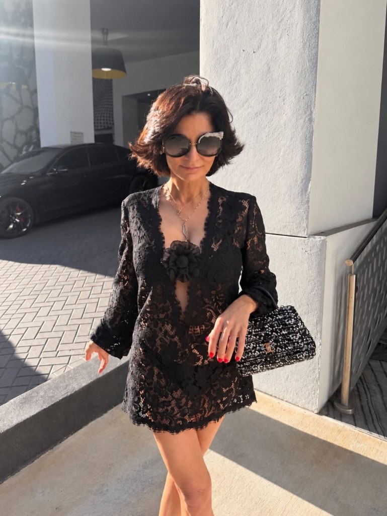 Julia Haart in a black lace dress and sunglasses, holding a Chanel bag.