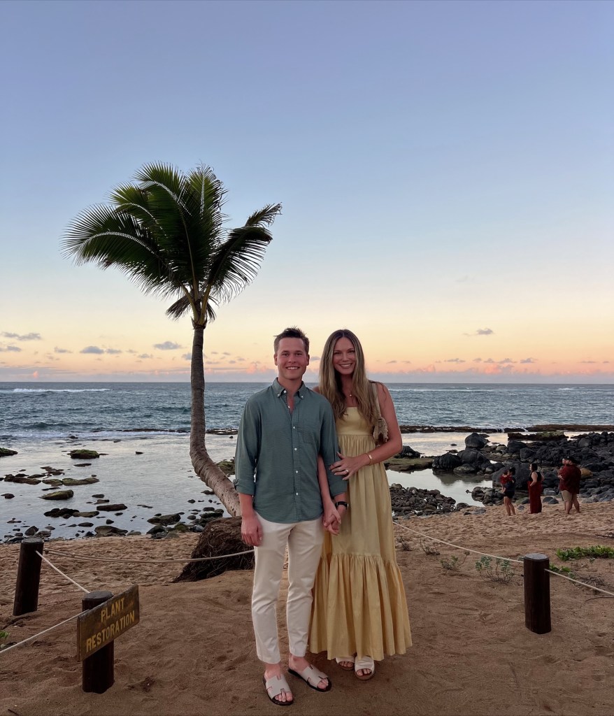 Lev Bure and wife Elliott Bure standing on a beach at sunset, holding hands.