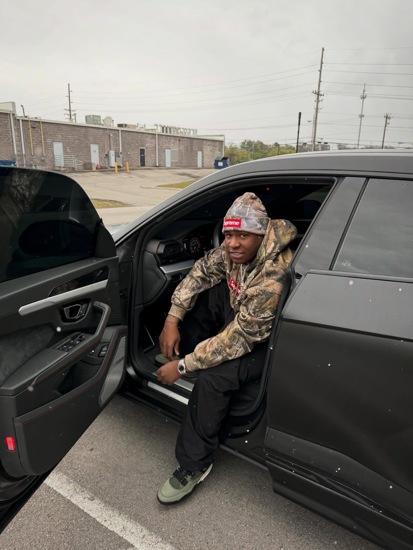 Tay Keith sitting in the open door of a black car.