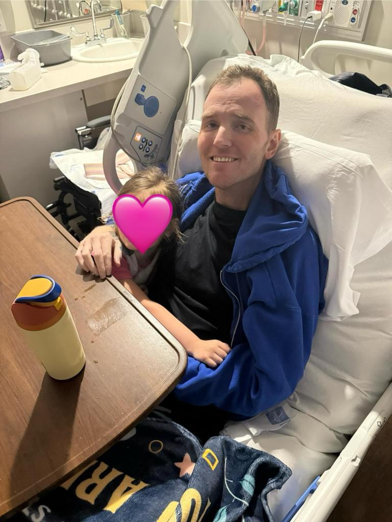 Chad Gilbert, musician from New Found Glory, smiles in a hospital bed with a child next to him.