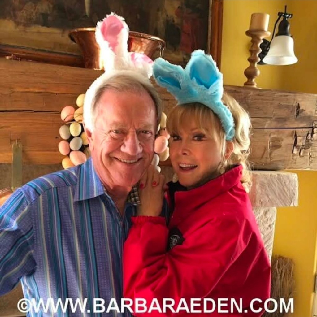 Barbara Eden and a man smiling while wearing bunny ears.
