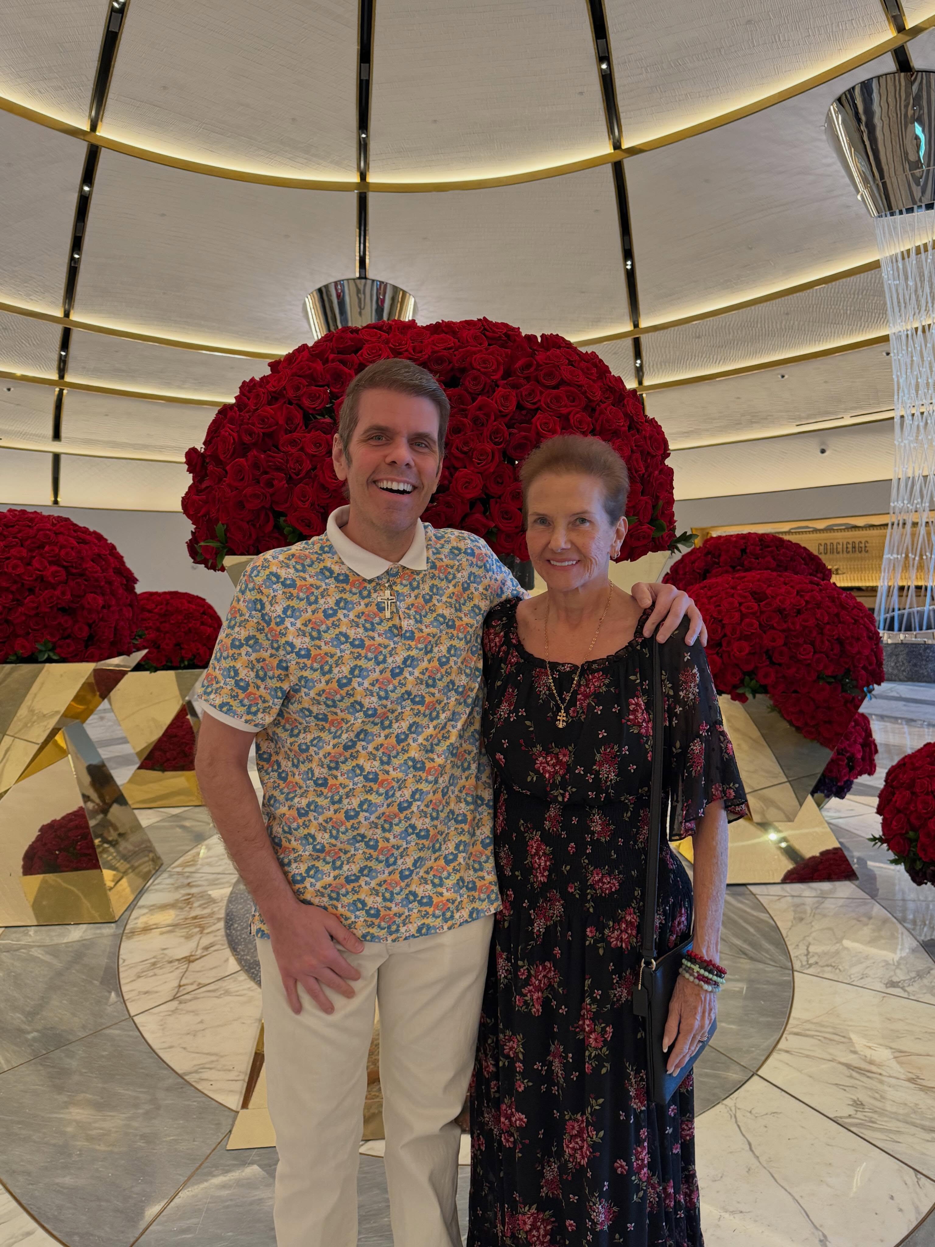 Perez Hilton and his mother, Mary, pose in front of a massive display of red roses.