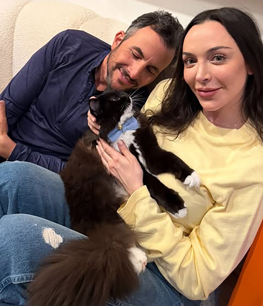 Farrah Brittany and Zach Goldsmith holding their black and white cat with a light blue collar.