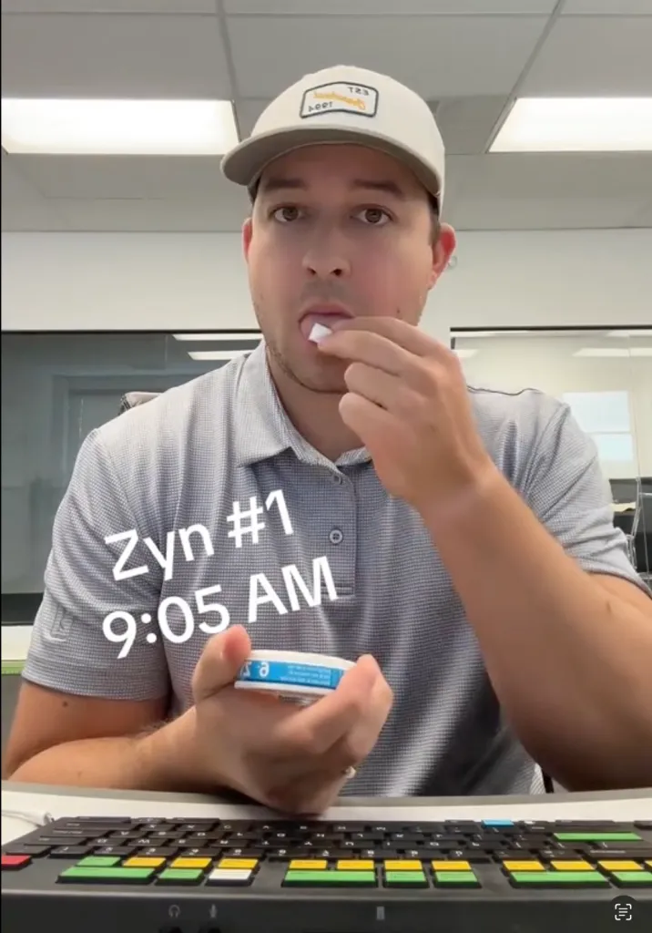 Nolan Borgersen placing a Zyn nicotine pouch in his mouth at 9:05 AM in an office setting.