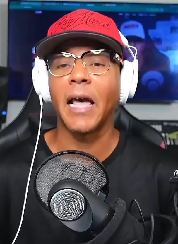 YouTuber Ray Marcel wearing a red cap, glasses, and white headphones, speaking into a microphone.