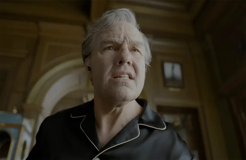 Tom Cruise, in aging make up, wearing black silk pajamas.