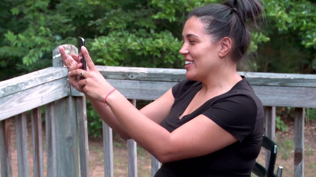 Amber Eggers smiling while holding her phone with a lit cigarette in her hand.