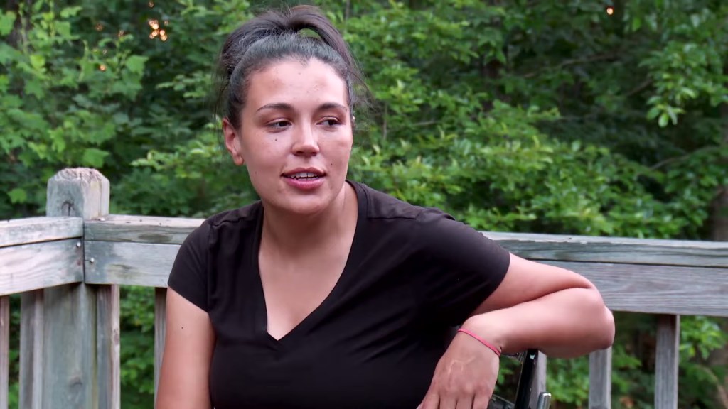 Amber Eggers, from Love After Lockup, sits outdoors on a wooden deck, her hair tied back, wearing a black shirt.