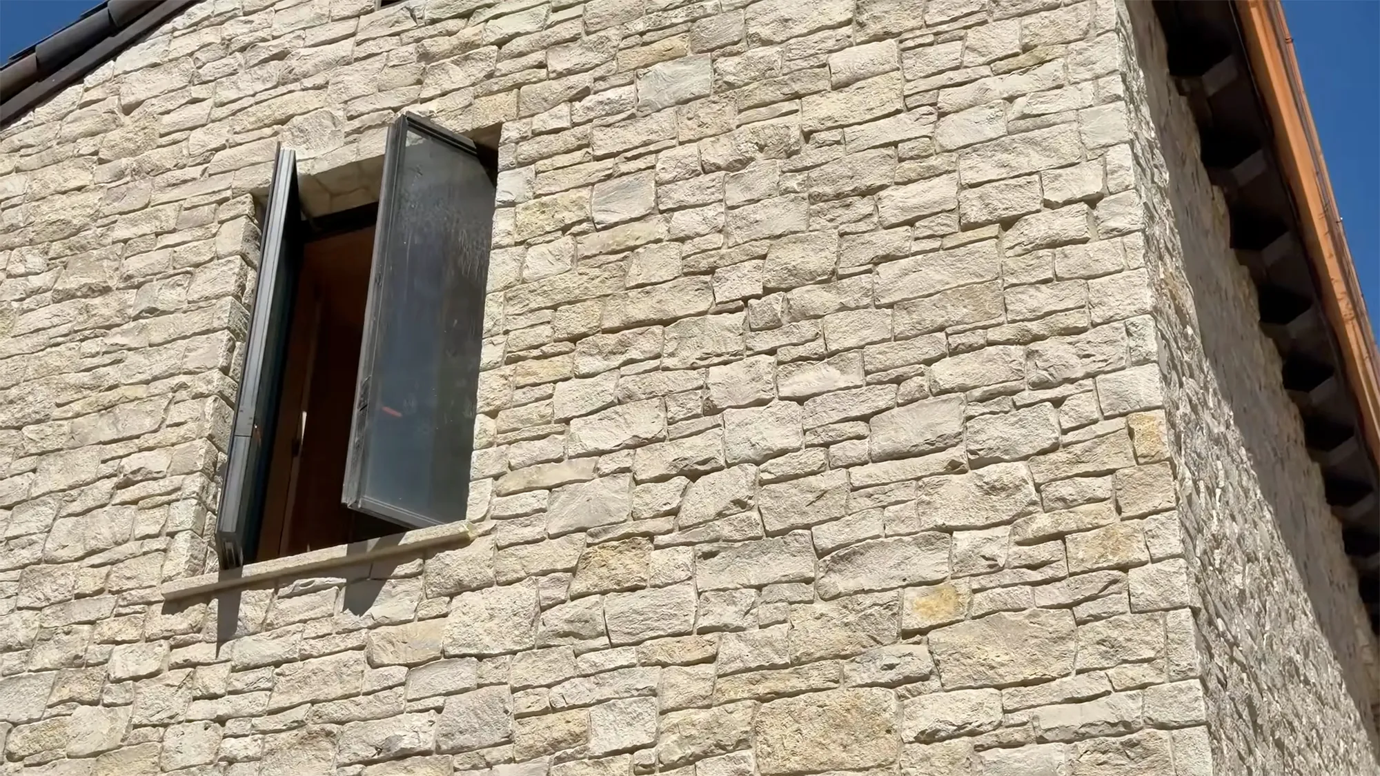 Side of a house under construction with a stone facade and an open window.