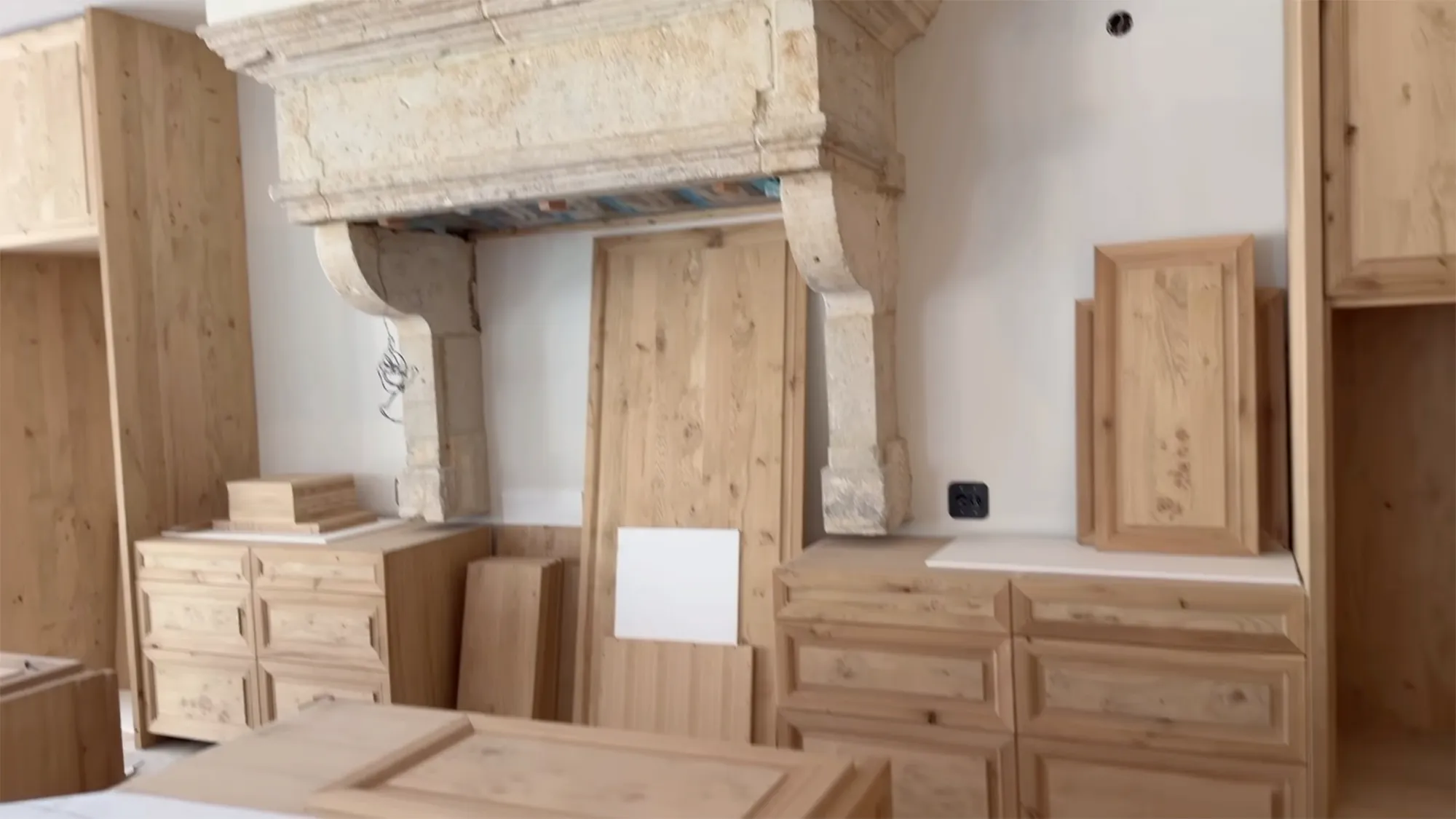 The interior of a house under construction shows unfinished wooden cabinets and a stone fireplace.