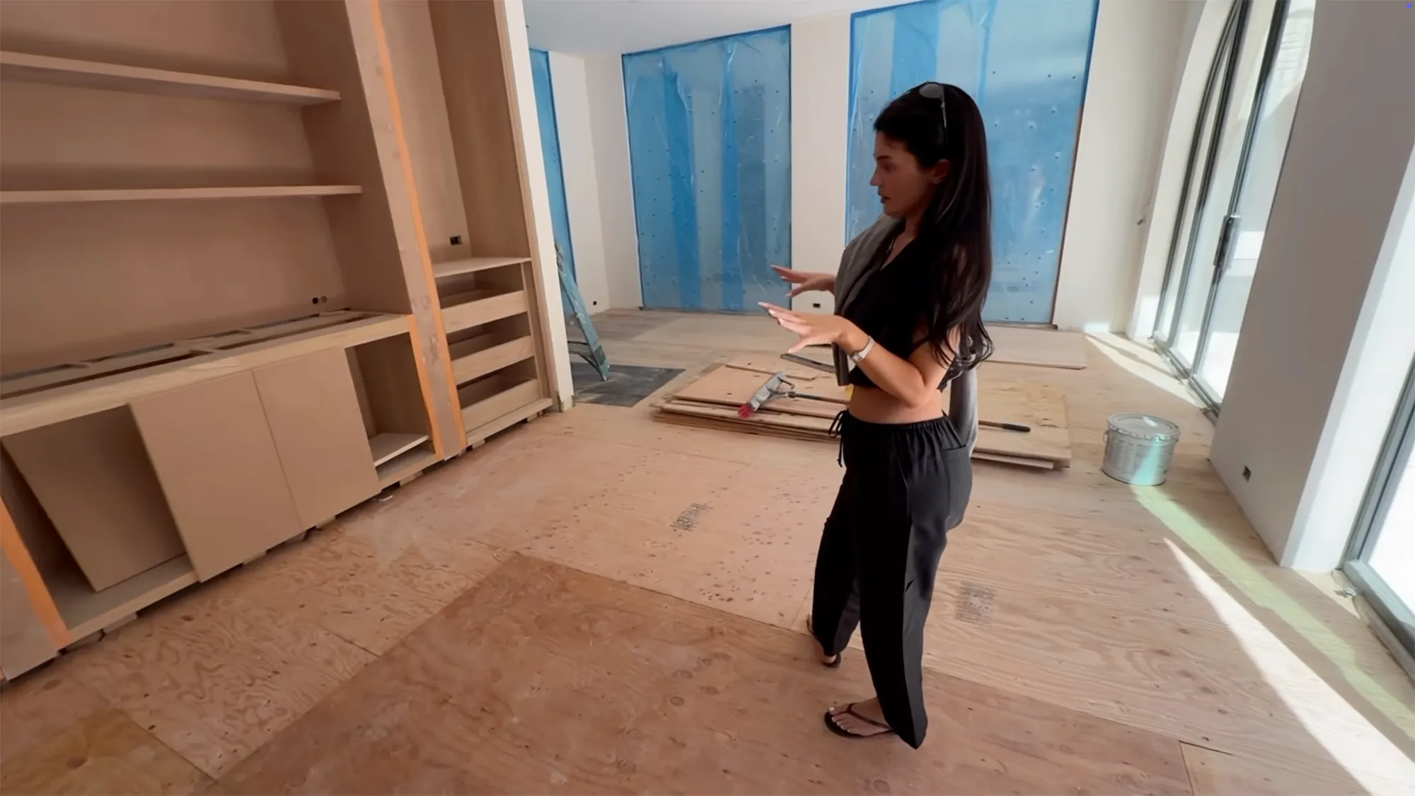 Kylie Jenner in her new home, which is under construction, with partially built wooden shelving and walls covered in blue sheeting.