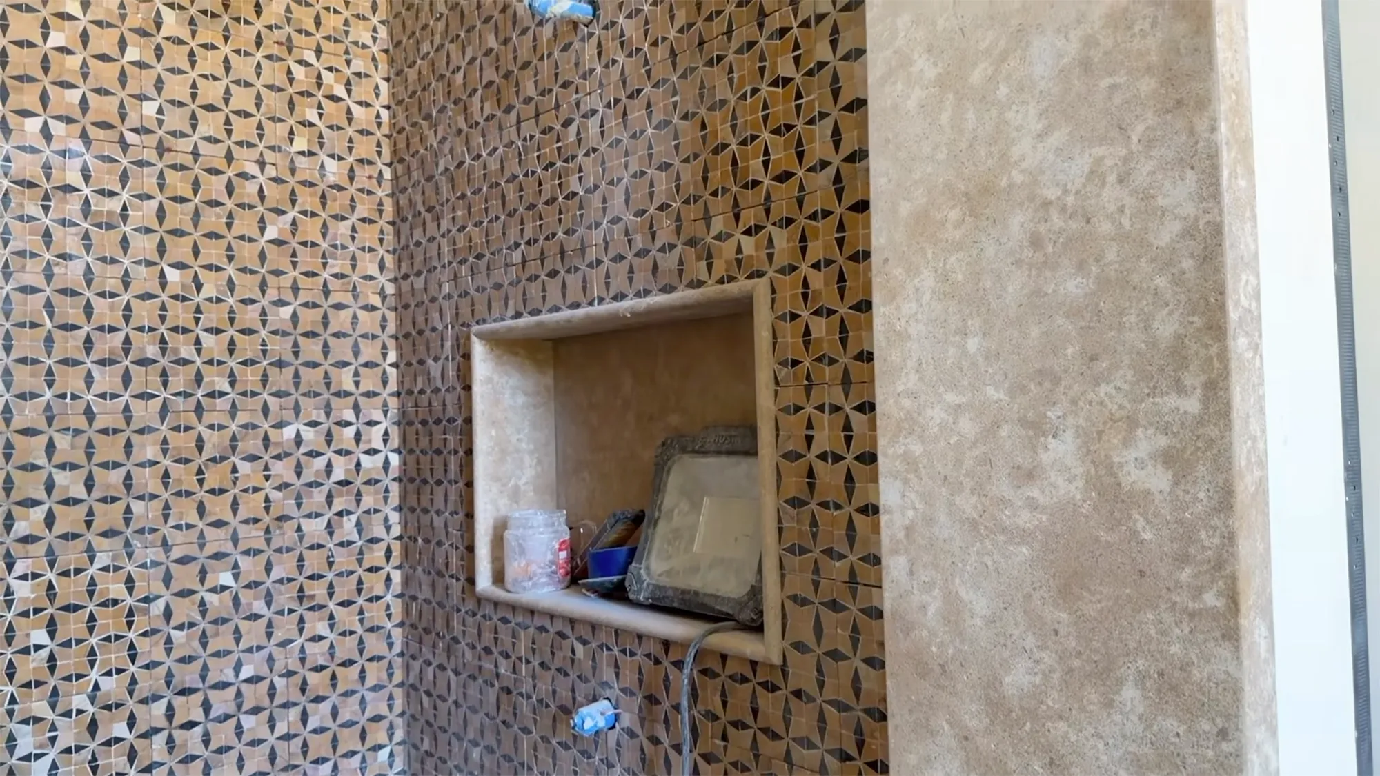 A tiled wall under construction featuring geometric patterns and a built-in niche.