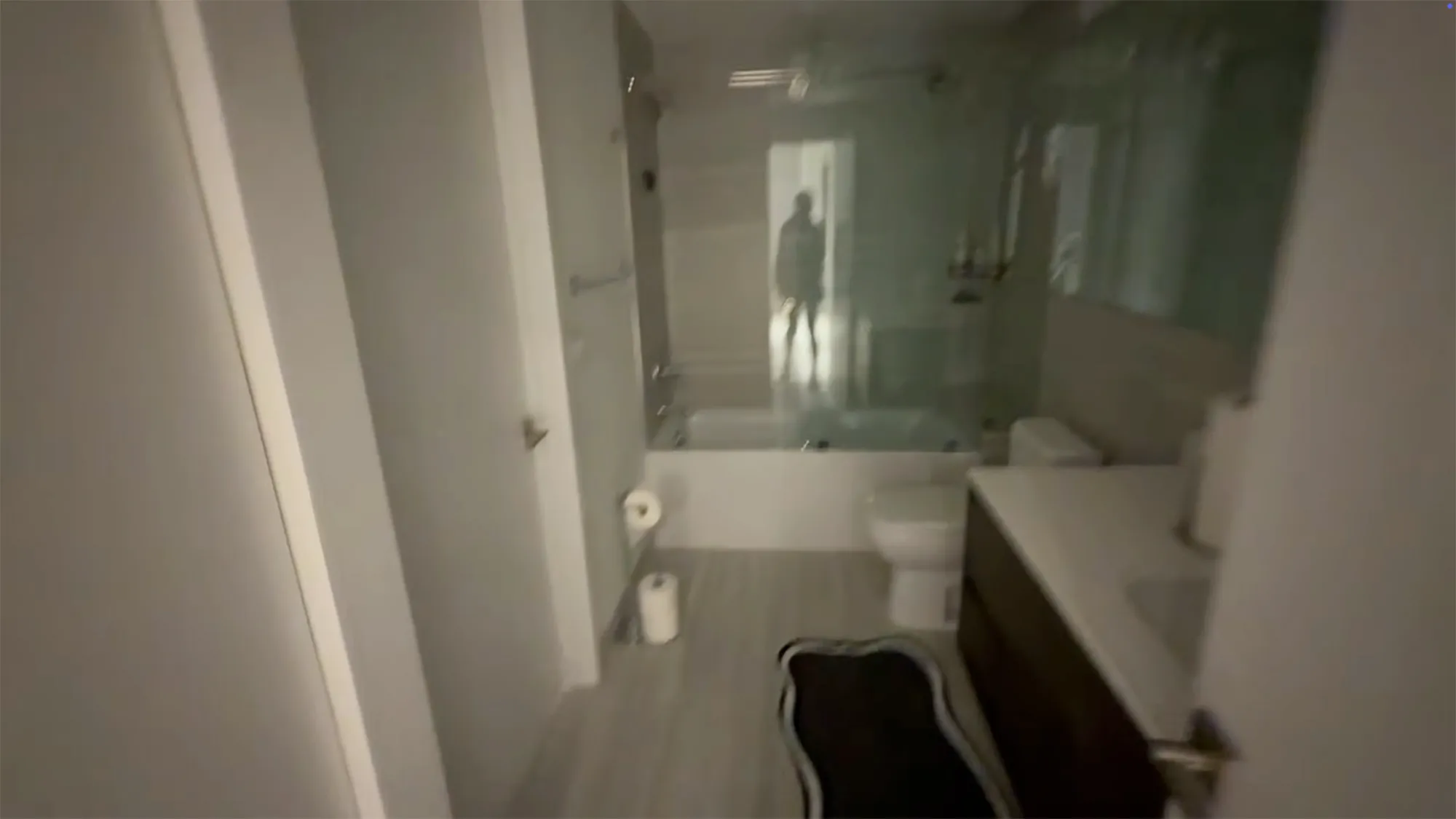A person's silhouette reflected in the glass shower door of a modern bathroom.